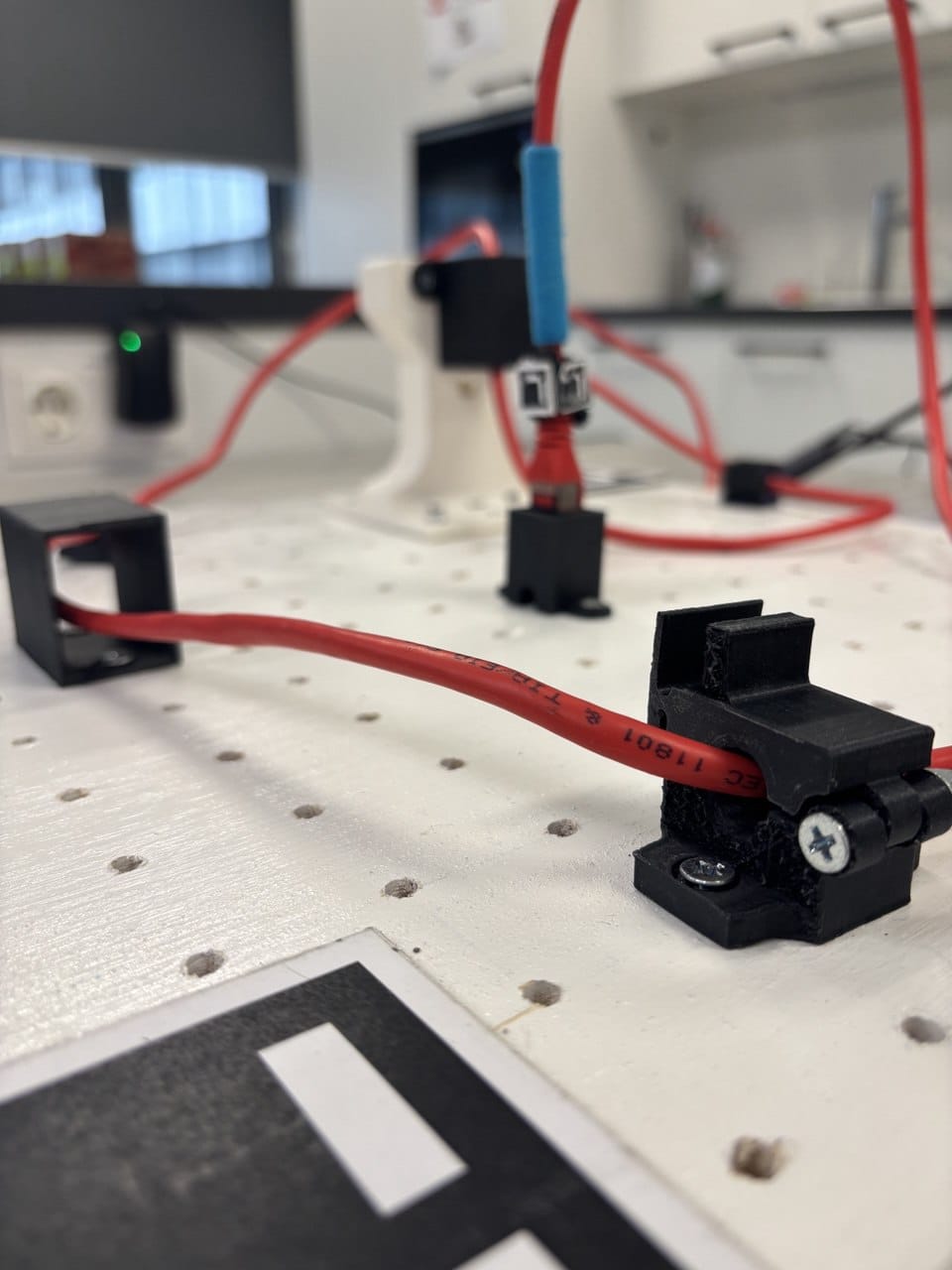 Red cable routed through printed clips on the perforated board.