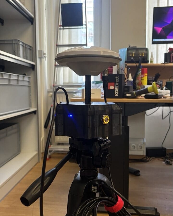 Assembled base station with GNSS antenna dome, mounted on a tripod in a lab.